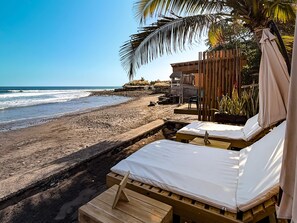 Alojamiento frente a la playa con camas de madera, una estructura de techo de paja y vista al océano.