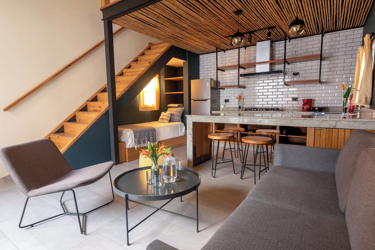 A modern kitchen with a built-in refrigerator, wooden staircase, and a dining area with stools.
