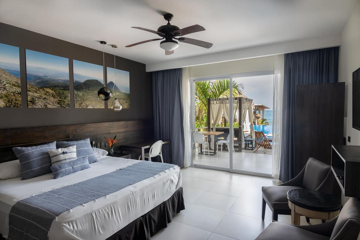 A modern bedroom with a large bed, a ceiling fan, and a view of a patio with outdoor seating.