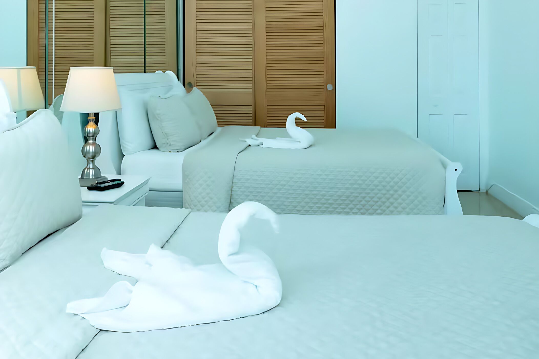 Une chambre d’hôtel avec deux lits, une table de chevet, une lampe et une serviette en forme de cygne.