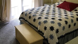 Ein Schlafzimmer mit einem Bett, einer Bank, einem Nachttisch, einer Lampe und einem Fenster mit Vorhängen.