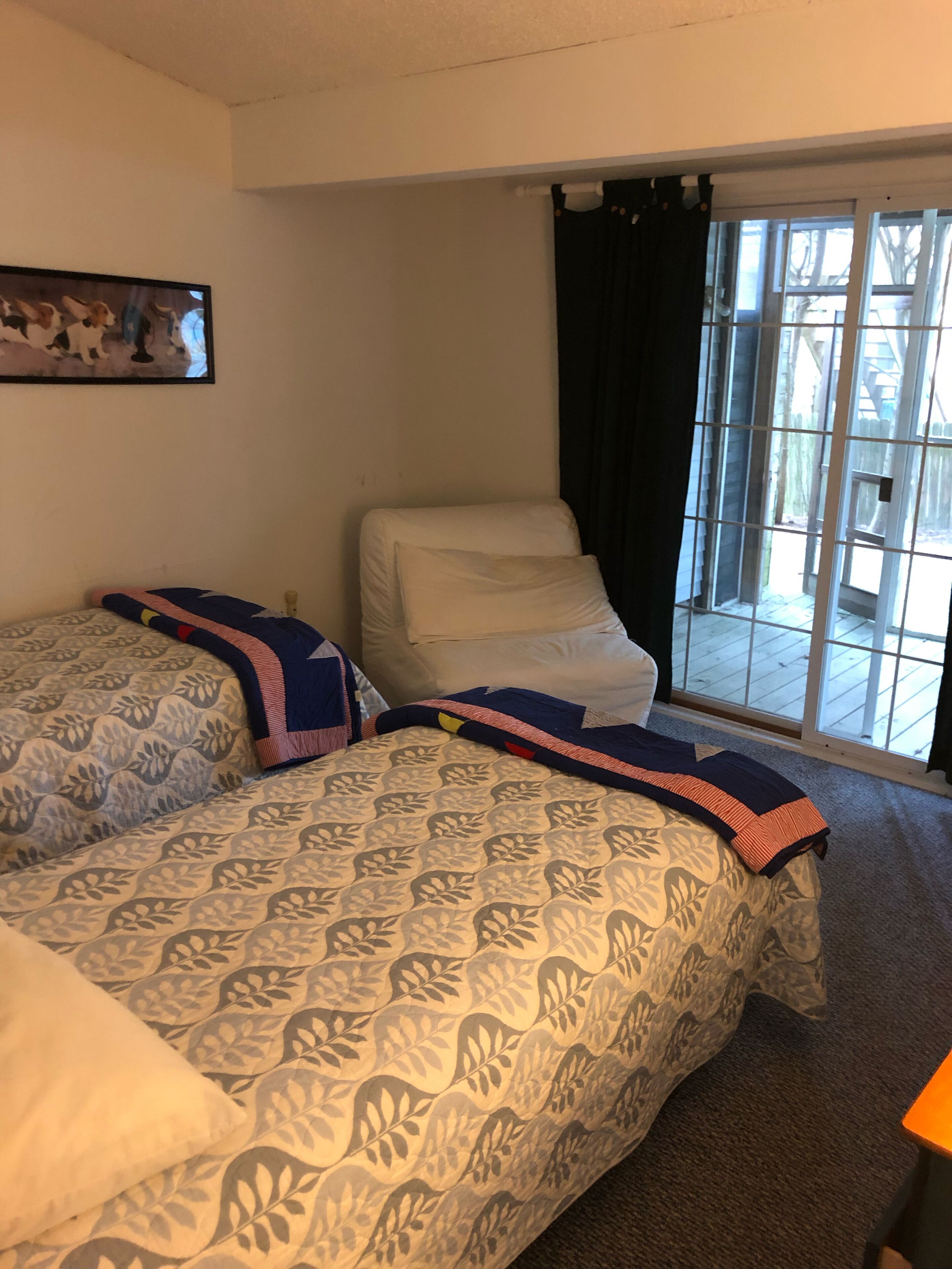 A bedroom with two beds, a window with curtains, and a door leading to an outdoor area.