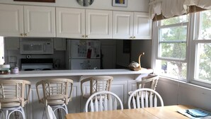 Eine Küche mit weißen Schränken, einer Mikrowelle, einem Kühlschrank und einem Essbereich mit weißen Stühlen und einem Holztisch.
