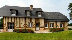 Una casa tradicional de entramado de madera con tejado inclinado, múltiples ventanas y un césped cuidado con flores rojas.