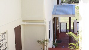 A two-story building with a red carpeted entrance, potted plants, and a small balcony with a metal roof.