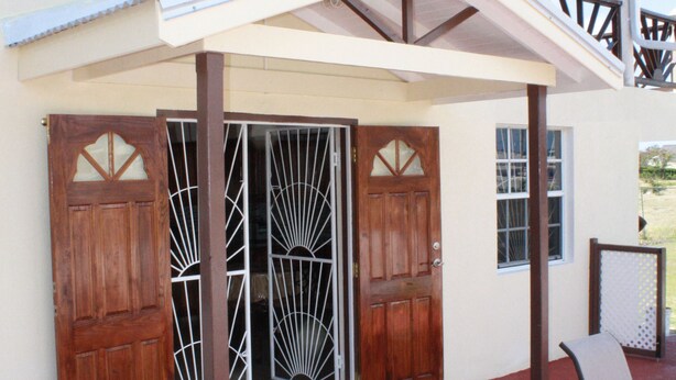 A two-story building with a covered patio area, a wooden door with a metal gate, and a chair.