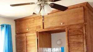 A bedroom with a bed, a wooden wardrobe with a mirror, and a ceiling fan.