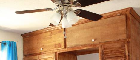Un dormitorio con una cama, un armario de madera con espejo y un ventilador de techo.