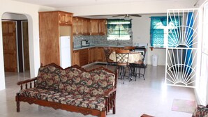 A living room with a sofa, a dining area with chairs and a table, and a kitchen with wooden cabinets and a refrigerator.