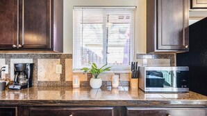 A kitchen with dark wooden cabinets, a granite countertop, a coffee maker, a microwave, and a window with blinds.