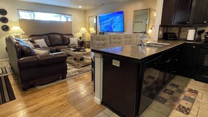 A modern kitchen with a central island, dark cabinetry, and a large window providing natural light.