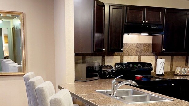 A modern kitchen with dark cabinets, a granite countertop, and a built-in island with bar stools.