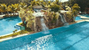 Una piscina con caída de agua rodeada de palmeras y una isla rocosa.