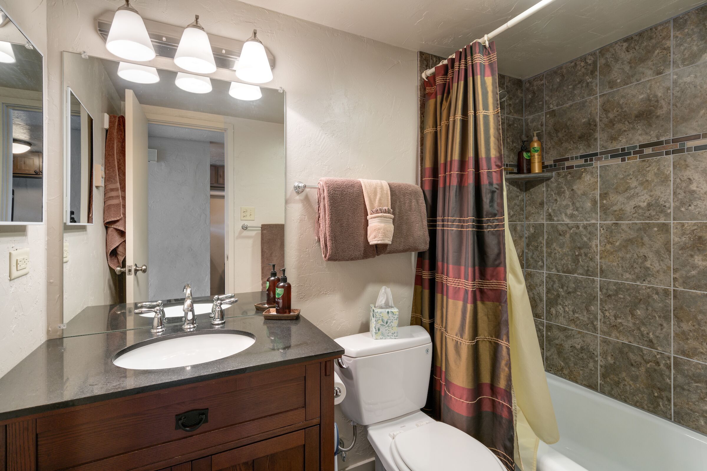 Une salle de bain équipée d’un lavabo, d’un miroir, de toilettes et d’un rideau de douche.