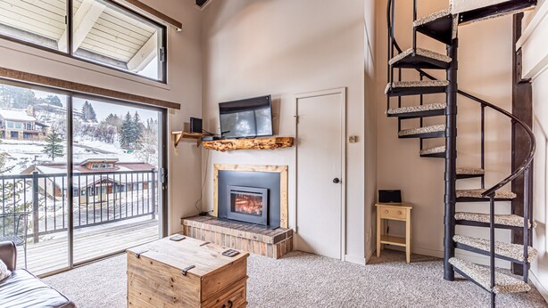 A spacious living room with a fireplace, a wooden coffee table, a sofa, and a spiral staircase. - Bright Loft Condo | Cathedral Ceilings, Fireplace, and Walk to Slopes! (Steamboat Springs)