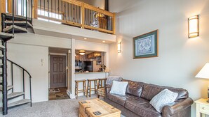 A spacious living area with a brown leather sofa, a wooden coffee table, and a staircase leading to an upper level. - Bright Loft Condo | Cathedral Ceilings, Fireplace, and Walk to Slopes! (Steamboat Springs)