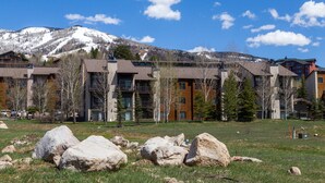 A modern hotel with multiple floors, large windows, and a view of snow-capped mountains in the background. - Bright Loft Condo | Cathedral Ceilings, Fireplace, and Walk to Slopes! (Steamboat Springs)
