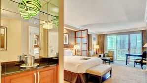 A hotel room with a large bed, a desk, a chair, a dining table, and a view of the city through large windows.