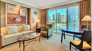 A hotel room with a large window, a sofa, a coffee table, a desk, and a chair.