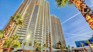 A high-rise hotel with multiple balconies, palm trees, and a clear sky.