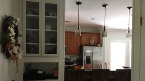 A kitchen with wooden cabinets, a stainless steel refrigerator, and hanging pendant lights.