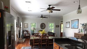 A spacious kitchen with wooden flooring, a dining area with a table and chairs, a refrigerator, a ceiling fan, and a sink.
