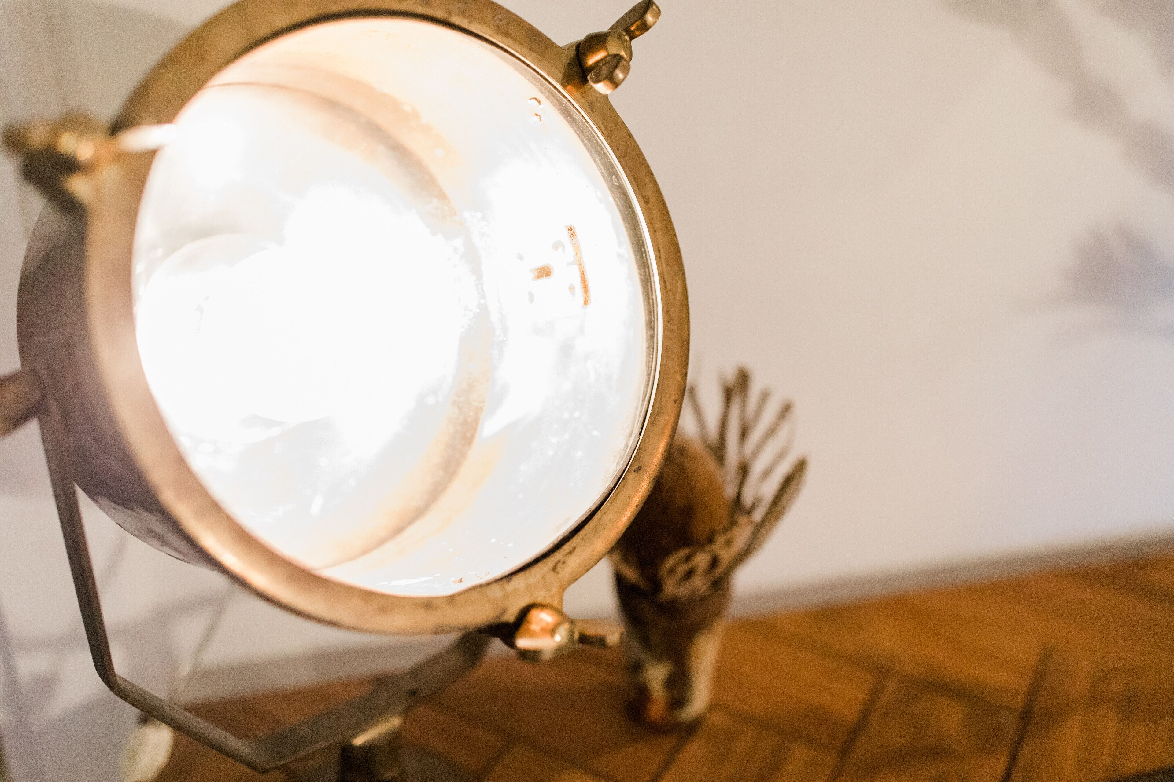 A close-up of a brass lamp with a white shade, a metal stand, and a decorative vase with branches in the background.