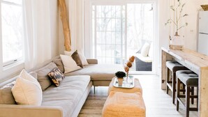 Un salon moderne avec un canapé, un pouf et un coin repas agrémenté de tabourets de bar.