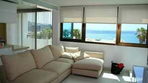 Una sala de estar moderna con un sofá seccional color beige, una mesa de centro de vidrio y vistas al océano a través de amplios ventanales.