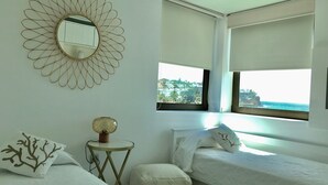 Un dormitorio con dos camas, un espejo redondo, una mesita pequeña y vistas al mar.