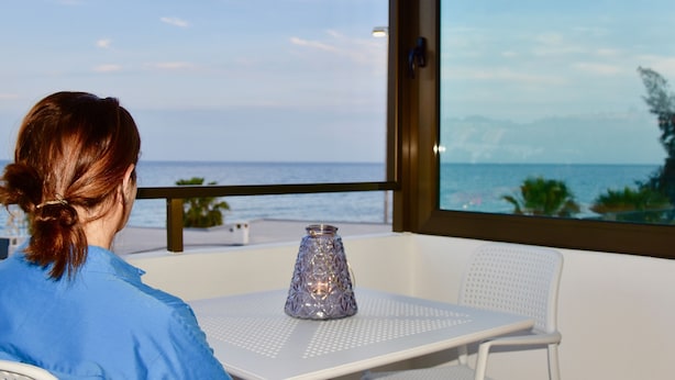 Una persona sentada a una mesa con vista al océano a través de un ventanal amplio.