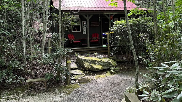 Una cabaña rústica de techo rojo, rodeada por un bosque denso.