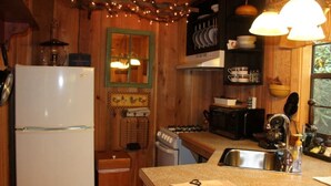 Una cocina compacta con paredes de madera, un refrigerador blanco, estufa y lavamanos.