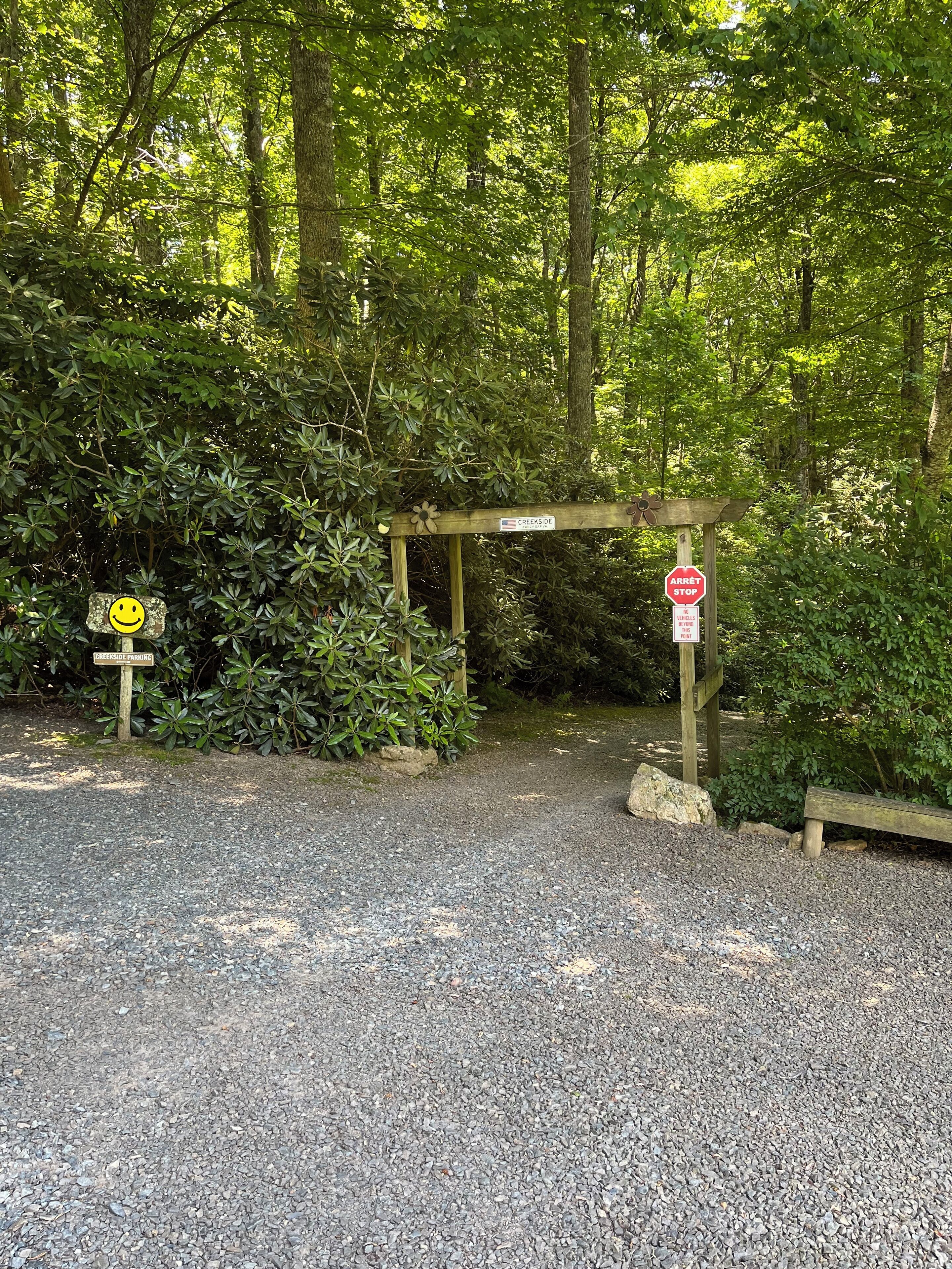 Een grindpad dat leidt naar een houten poort met een stopbord en een bord waarop 'Creekside Parking' staat.