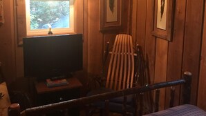 Una habitación de cabaña de madera con cama, escritorio, silla y ventana con cortinas.
