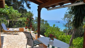 Un espace extérieur abrité, doté d’un sol en pierre, de mobilier en osier et offrant une vue sur la mer.