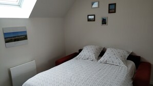 A bedroom with a bed, a radiator, a skylight, and three framed pictures on the wall. - Cozy studio near Caen and the sea, landing beaches (Biéville-Beuville)