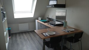 A compact kitchen with a window, a built-in oven, a microwave, and a stainless steel refrigerator. - Cozy studio near Caen and the sea, landing beaches (Biéville-Beuville)