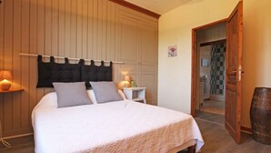 Une chambre à coucher comprenant un lit, des tables de chevet, une commode, une armoire en bois et une porte donnant sur une salle de bain.