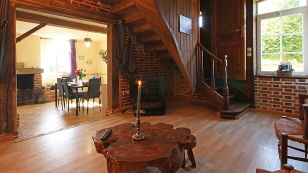 Un intérieur rustique avec des murs en briques apparentes, un escalier en bois, une cheminée et un coin repas.