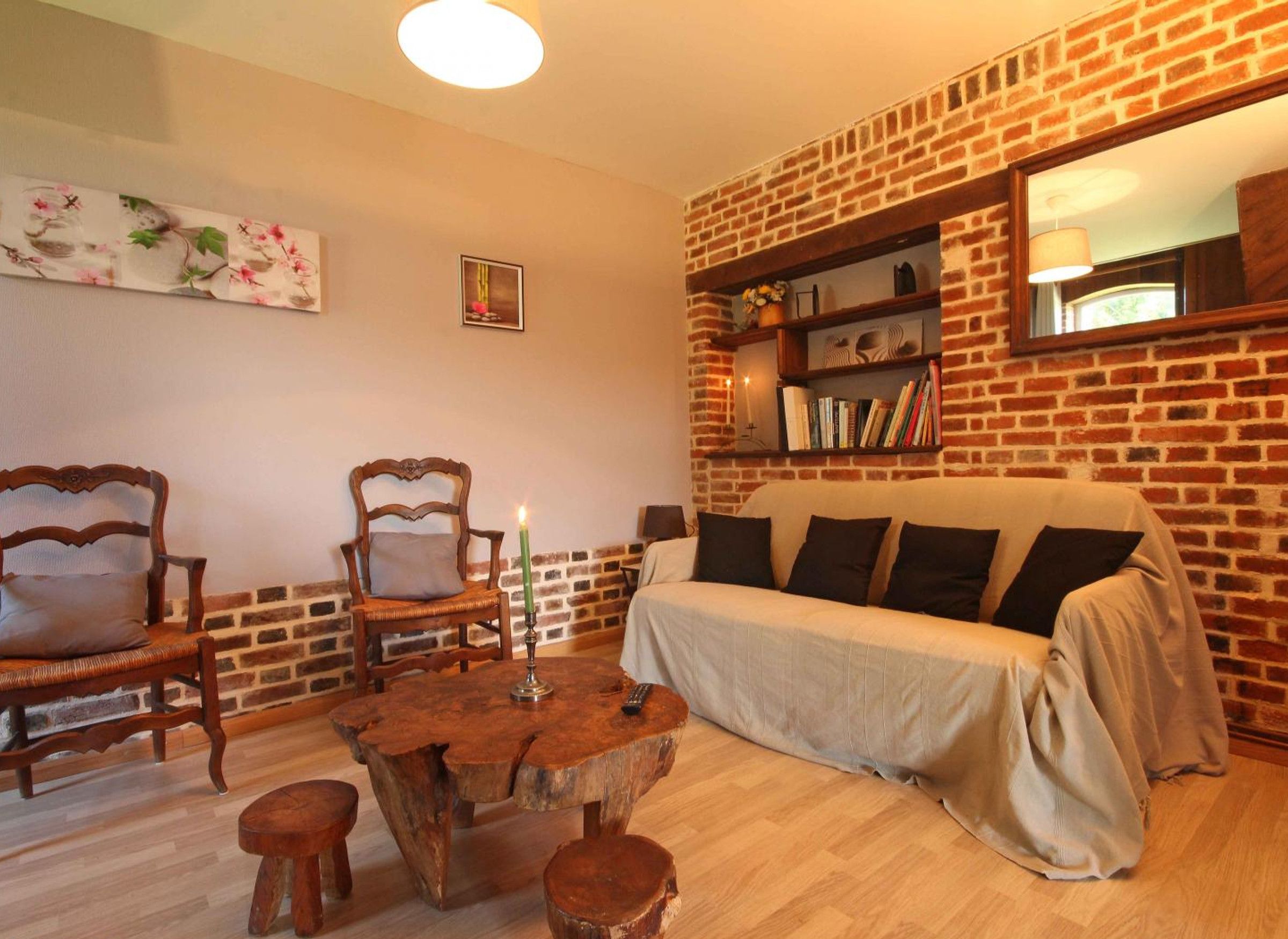 Een gezellige woonkamer met een bakstenen muur, een bank, twee fauteuils, een houten salontafel en een boekenplank.