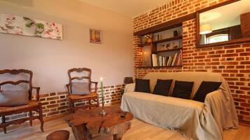 Een gezellige woonkamer met een bakstenen muur, een bank, twee fauteuils, een houten salontafel en een boekenplank.