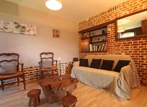 Un salon chaleureux avec un mur en briques, un canapé, deux fauteuils, une table basse en bois et une bibliothèque.