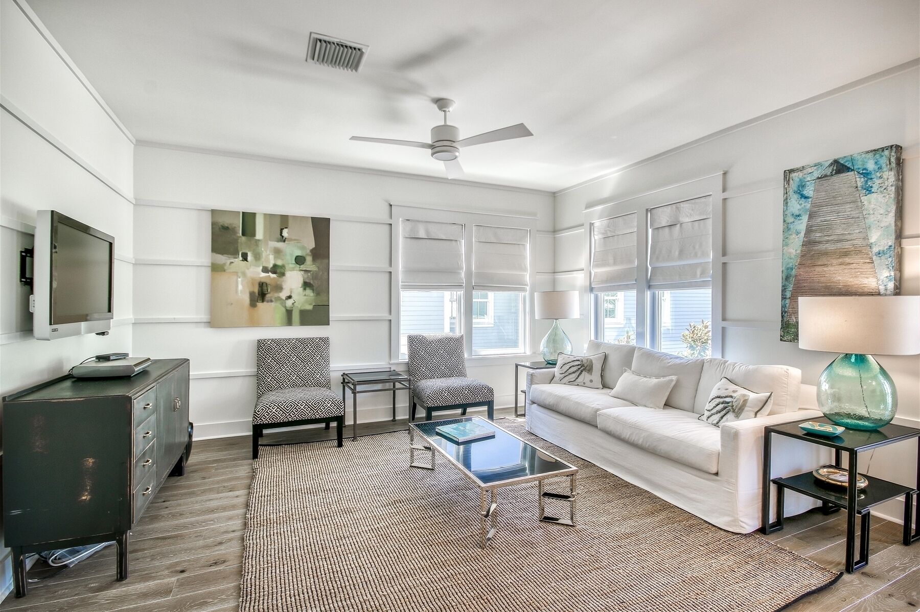 A modern living room with a white sofa, patterned armchairs, a glass coffee table, and a dark wooden cabinet.