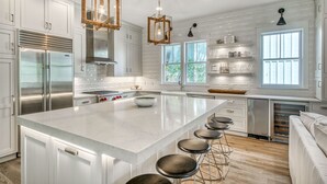 Een moderne keuken met witte kasten, een groot eiland met krukken, roestvrijstalen apparatuur en hanglampen.