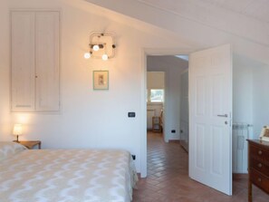 A bedroom with a bed, a bedside lamp, a wall-mounted light fixture, a door, and a hallway leading to another room. - Michelangelo II by Interhome (Marina Pietrasanta)