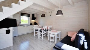 A modern kitchen with white cabinets and a dining area with white chairs and a table. - White cottage Lux, Grzybowo in Kołobrzeg, 1-6 persons, with air conditioning (Grzybowo)