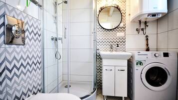 A modern bathroom with a shower, a sink, a mirror, and a washing machine.