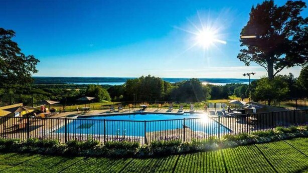 A swimming pool with a view of the ocean, surrounded by a fence and greenery. - Year round fun close to lakes, golf, and ski! (Bellaire)