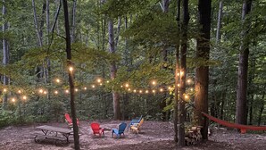 A forested campsite with string lights, a hammock, and several chairs. - Year round fun close to lakes, golf, and ski! (Bellaire)